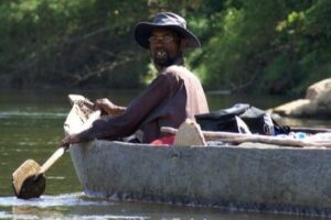 A man in a hat is paddling a wooden canoe.